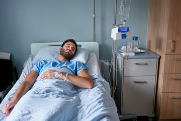 Man asleep in a hospital bed attached to a drip