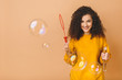 © denis_vermenko - Beautiful brunette curly student girl wears casual making soap bubbles isolated on beige background.