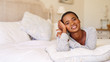 © marvent - Smiling young woman lying on her bed at home