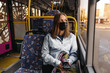 © sushytska - Coronavirus, covid 2019, young woman with respiratory mask traveling in the public transport by bus
