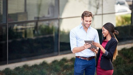 Wall Mural - Smiling diverse businesspeople using a tablet together outside