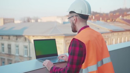 Wall Mural - On balcony man engineer stand using laptop computer with green screen worker project occupation builder technology mock-up professional male safety device computer slow motion