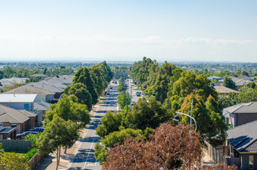 Wall Mural - A main road in Melbourne's suburb lined with green trees and residential houses on sides. Elevated view of Australian homes. Copy space for text. Point Cook, VIC Australia.