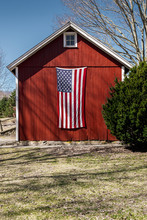 United States Flag Hanging On An Old New England Red Barn In The Spring Time