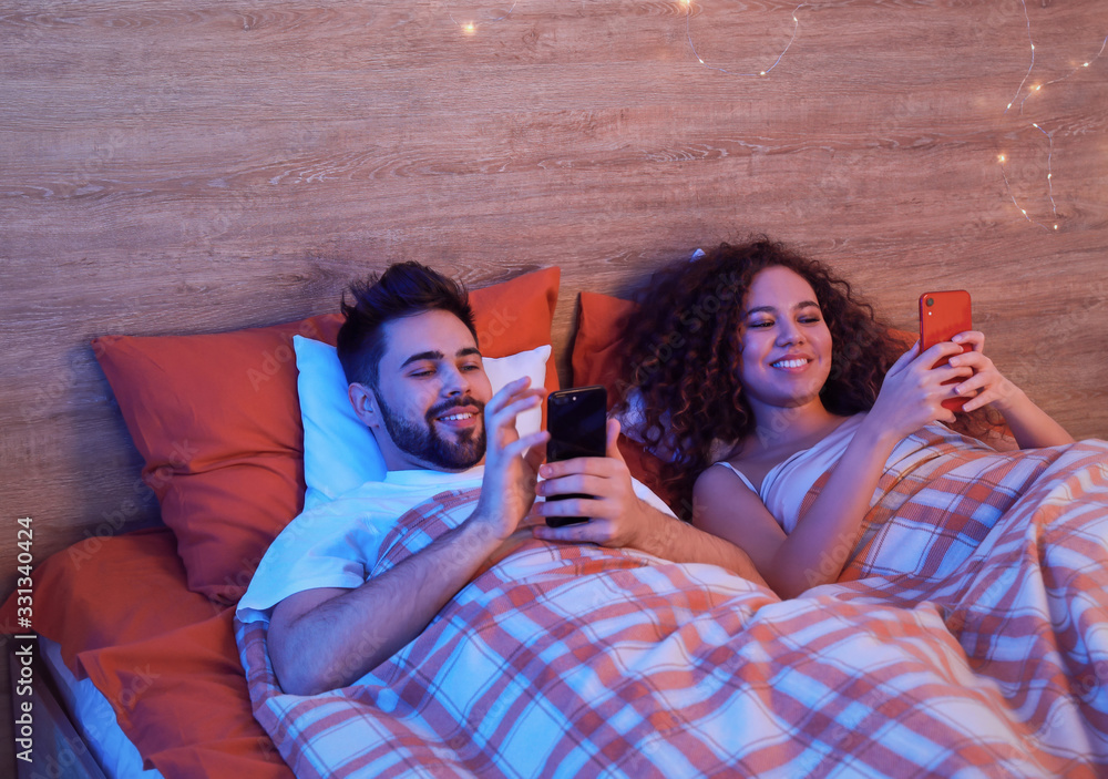 Happy young couple with mobile phones in bedroom