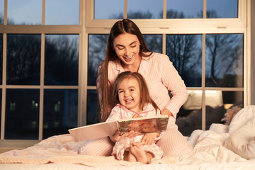 Wall Mural - Mother and her little daughter reading bedtime story at home