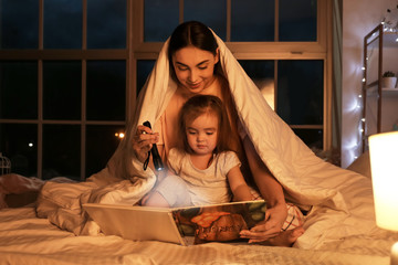 Wall Mural - Mother and her little daughter reading bedtime story at home