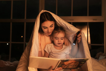 Wall Mural - Mother and her little daughter reading bedtime story at home