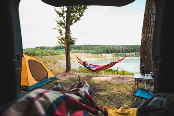 Wall Mural - person view couple resting at camping woman laying in hammock with beautiful view of forest lake