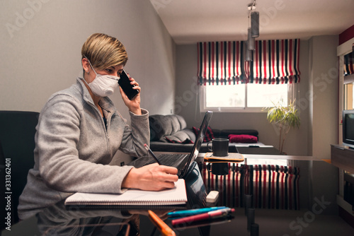 Concept: Woman in voluntary confinement with a surgical mask for the prevention of the coronavirus covid virus19. She works at home using the dining room table as a desk with a laptop.