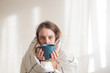 © lamapacas - Ill woman under white blanket drinking tea on white background. Illness treatment, home isolation, quarantine. Copy space