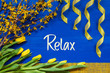 © Nelos - English Text Relax. Yellow Spring Flowers Like Tulip And Branches. Festive Decoration With Ribbon. Blue Wooden Background