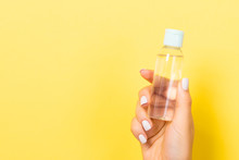 Female Hand Holding Cosmetics Bottle At Yellow Background With Empty Space For Your Design