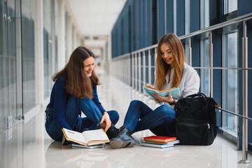 Wall Mural - two pretty female students with books sitting on the floor in the university hallway