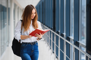 Wall Mural - Portrait of a pretty female student with books and a backpack in the university hallway