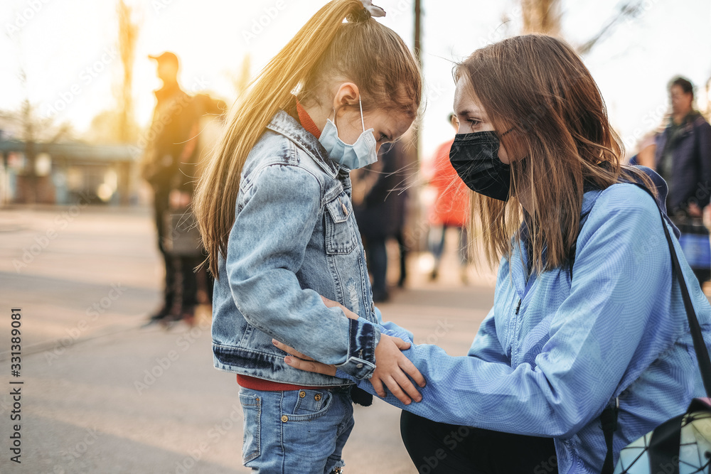 A girl with a child is standing on the road in a protective medical mask. Dangerous virus infection. Coronovirus in Europe - obrazy, fototapety, plakaty 