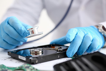 A male repairman wearing blue gloves holding stethoscope on hard drive from computer laptop in hands. Performs fault diagnostics and performs urgent repairs recovery lost data during deletion closeup