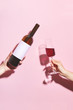 Hands holding a glass of wine and a bottle on pink background. Glass of  wine in female hand. Party insta time.