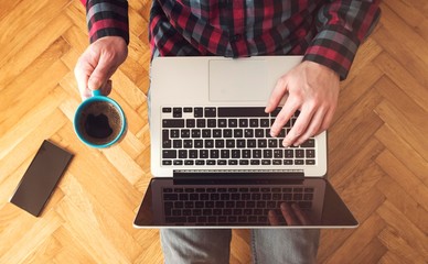 Top view of man using laptop. Coffee cup in hand.