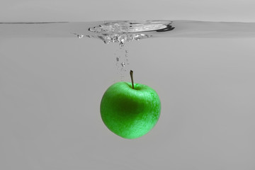 green apple falls into an aquarium with water on a gray background