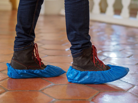 Wall Mural - Man with blue shoe covers worn over boots with red shoe laces standing on a tiles, closeup side view.