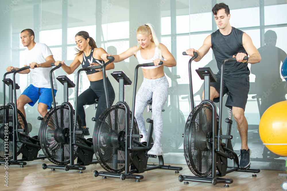 Group of young people doing exercises on elliptical machine at gym - obrazy, fototapety, plakaty 