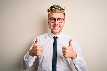 Young handsome caucasian business man wearing golden crown over isolated background success sign doing positive gesture with hand, thumbs up smiling and happy. Cheerful expression and winner gesture.