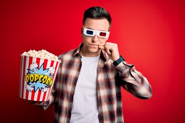 Wall Mural - Young handsome caucasian man wearing 3d movie glasses and eating popcorn mouth and lips shut as zip with fingers. Secret and silent, taboo talking