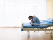 © MergeIdea - Asian patient young guy headache from migraine disease and mental stress while sitting and get intravenous therapy from professional doctor and nurse on hospital bed admit in clean room
