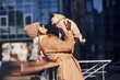 © standret - Woman in warm clothes have holding her little pug dog on hands near business building that on background