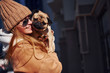 © standret - Woman in warm clothes have holding her little pug dog on hands near business building that on background