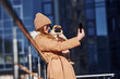 © standret - Woman in warm clothes have holding her little pug dog on hands near business building that on background and taking selfie