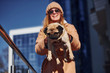 © standret - Woman in warm clothes have holding her little pug dog on hands near business building that on background