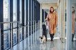 © standret - Young female passenger in warm clothes walking with her dog in airport hall