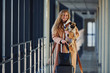 © standret - Young female passenger in warm clothes walking with her dog in airport hall