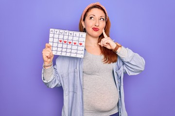 Sticker - Young beautiful redhead pregnant woman expecting baby holding period calendar serious face thinking about question, very confused idea