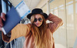 © standret - Young female passenger in warm clothes showing tickets in airport hall