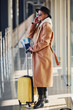 © standret - Young female passenger in warm clothes with tickets and baggage in airport hall