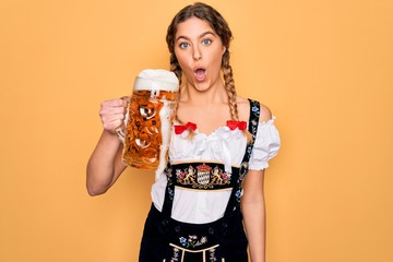 Wall Mural - Beautiful blonde german woman with blue eyes wearing octoberfest dress drinking jar of beer scared in shock with a surprise face, afraid and excited with fear expression