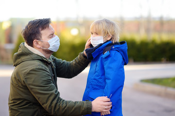 Mature man wearing a protective mask puts a face mask on a his son in airport, supermarket or other public place. Safety during COVID-19 outbreak.