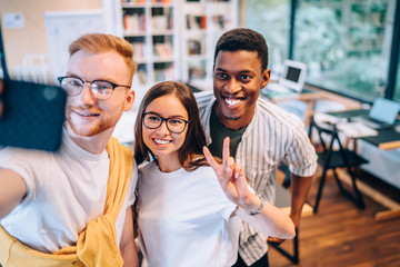 Wall Mural - Cheerful coworkers gesturing and taking selfie in office