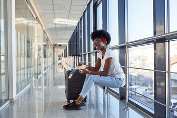 Young african american female passanger in casual clothes is in airport with baggage eating some food