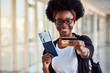 Young african american female passanger in casual clothes is in airport holding tickets and credit card