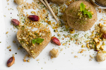 Traditional Turkish Semolina Halvah,shaped with a scoop on white with pistachio nuts and diced hazelnuts and fresh mint leaf.