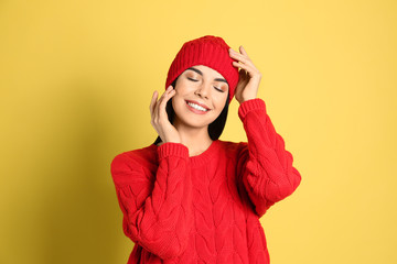 Canvas Print - Young woman wearing warm sweater and hat on yellow background. Winter season