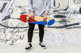 Close up of unrecognizable young man holding skateboard in the park .