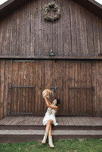 Photo Of The Beautiful And Sexy Blond Woman In Village, Sitting On The Stairs In Front Of Wooden Barn And Playing With Big Red Cat. Woman In Stylish Boho Casual Clothes Relaxing Near The Wooden Barn