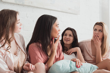 Wall Mural - Multicultural women talking and looking at each other with pillow on bed at bachelorette party