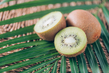 Wall Mural - Juicy kiwi fruit over palm leaves on rattan background. Copy space. Tropical travel, exotic fruit. Vegan and vegetarian concept