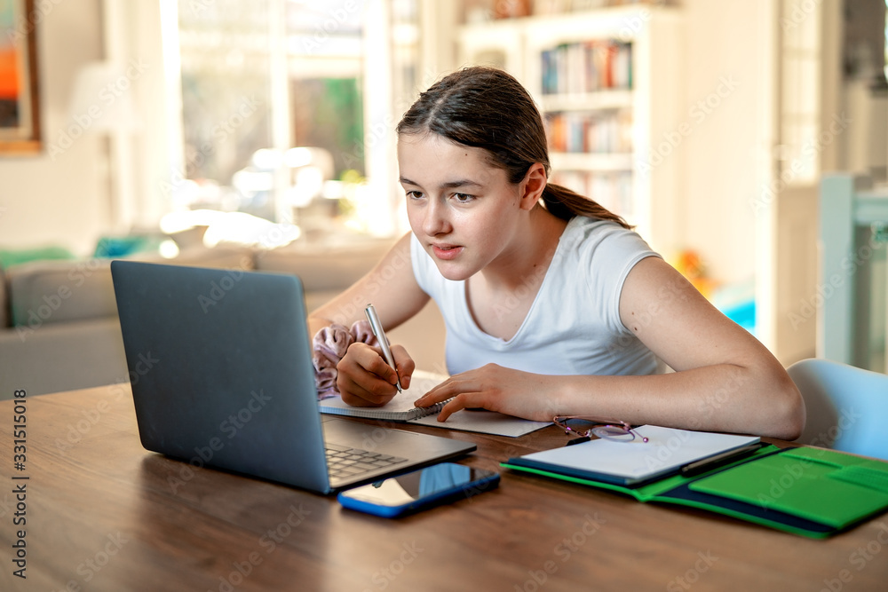 Teenager girl studying online at home looking at laptop at  quarantine isolation period during pandemic. Home schooling. Social distancing. Online school test. - obrazy, fototapety, plakaty 